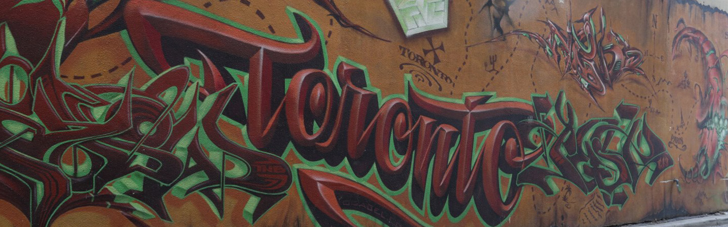 Large graffiti mural. The background of the mural resembles an old treasure map with an X marking the spot and the word "Toronto" below it. Painted over the map, the mural also features large stylized designs and a large scale stylized painting of the name "Toronto" in green and burgundy.